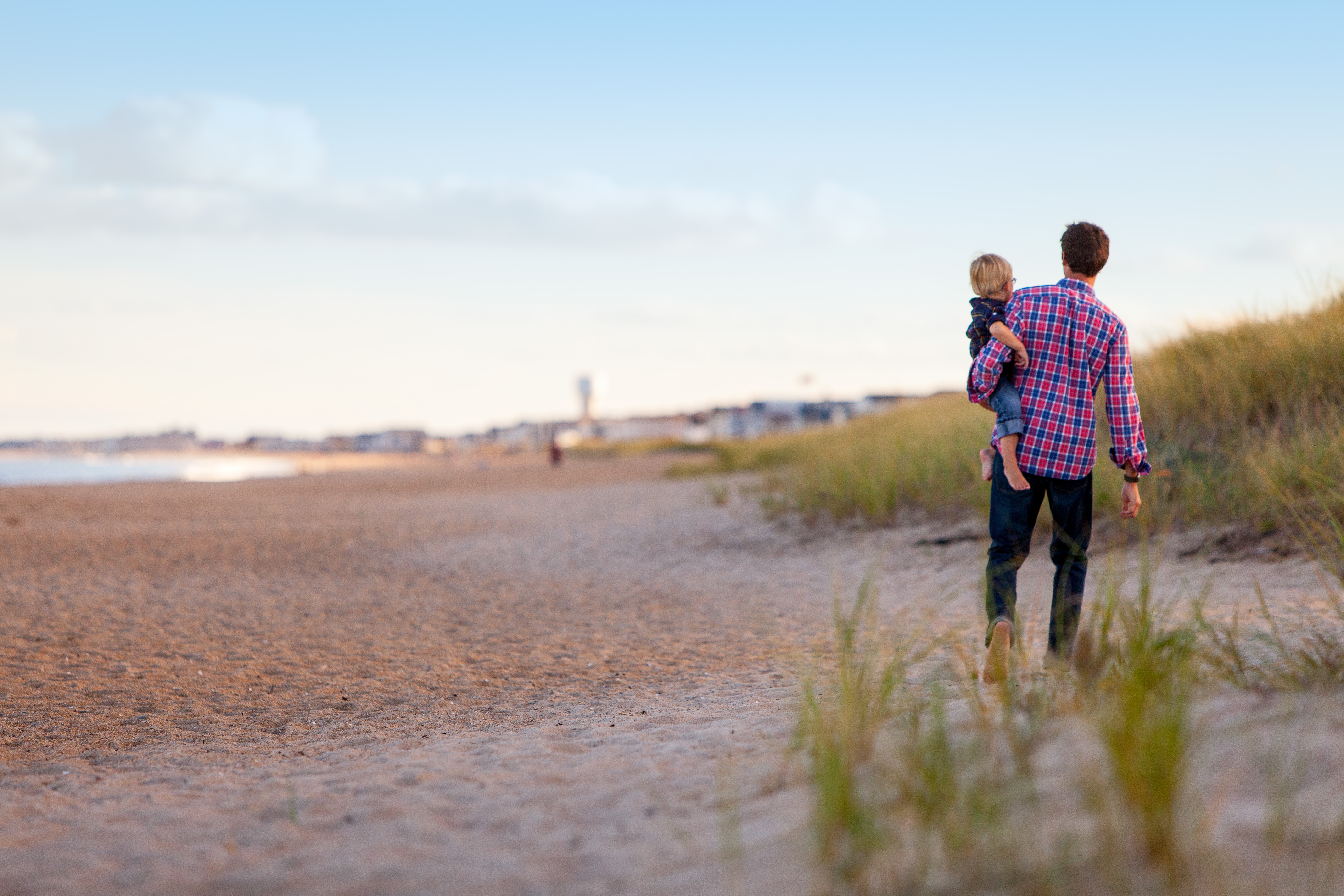 A father carrying his young son on a sandy beach