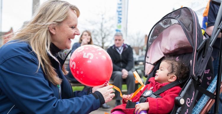 A volunteer handing a balloon over to a young child in a pram. 