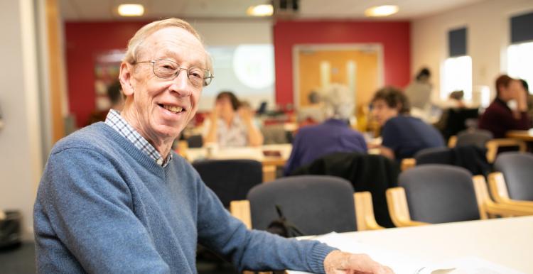 An older man sitting joyfully at a table in a communal space with other elderly patients. 