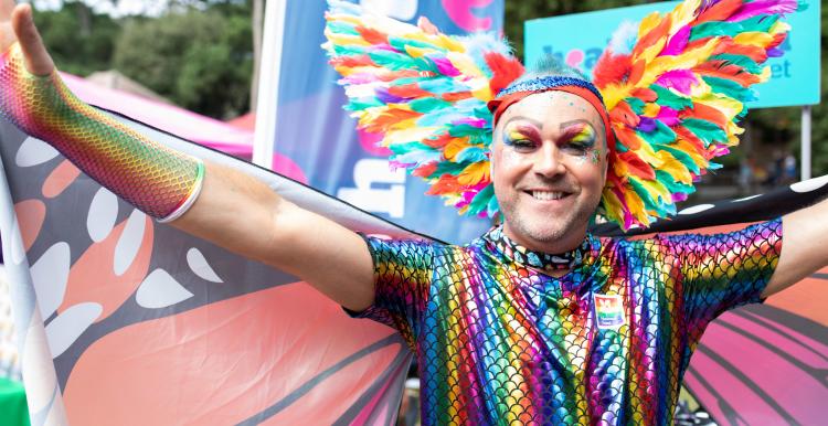 A person dressed as a rainbow butterfly, spreading their wings at a pride festival