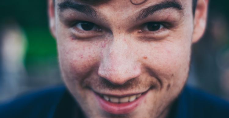 A close up of a brunette man smiling at the camera. 