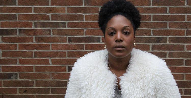 Woman in a teddy bear coat standing in front of a red brick wall.