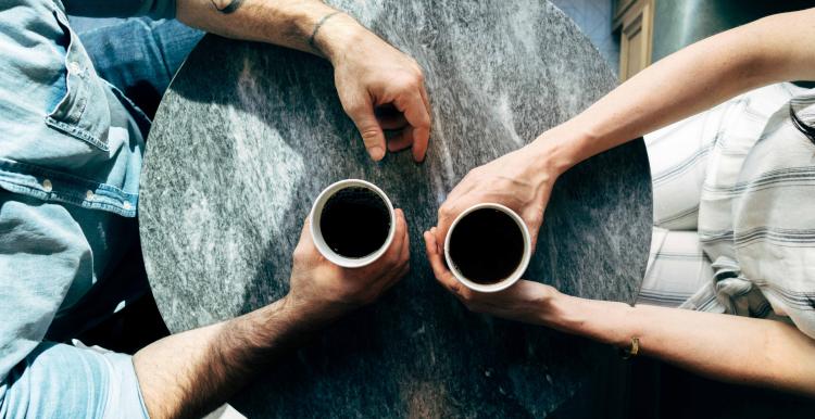 Two people sitting at a coffee table with there arms over the table.