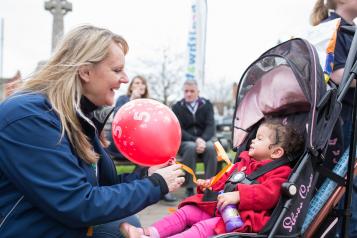 A volunteer handing a balloon over to a young child in a pram. 