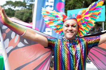 A person dressed as a rainbow butterfly, spreading their wings at a pride festival