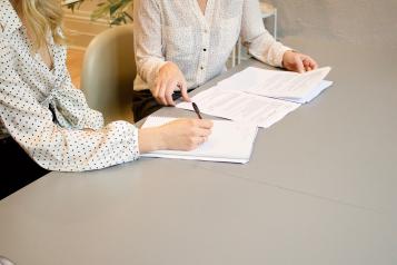 Two people talking over a document. They are sitting at a large table.