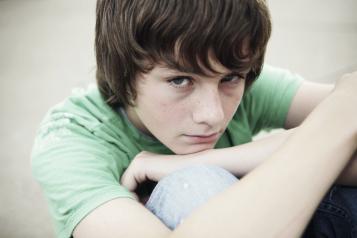 Young boy sitting down hugging his knees