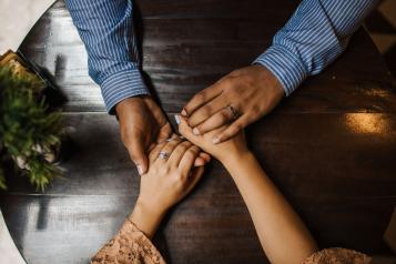 A husband and wife holding hands over a wooden table.