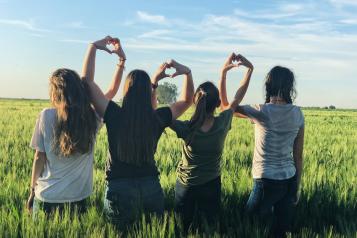 Four girls standing in a field using their hands to make hearts.