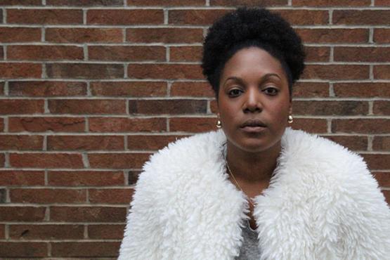 Woman in a teddy bear coat standing in front of a red brick wall.